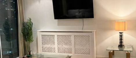 Una sala de estar moderna con una televisión de pantalla plana montada en la pared, una mesa de centro de vidrio, un sofá gris y piso de madera.