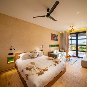 Une chambre d’hôtel avec un lit, un ventilateur de plafond, une fenêtre avec des rideaux, une petite table et une chaise.