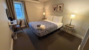 A hotel room with a bed, desk, chair, and two bedside lamps.