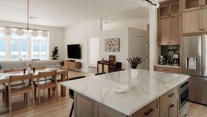 A modern kitchen with a large island, wooden cabinets, and a stainless steel refrigerator.