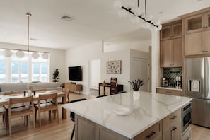 A modern kitchen with a large island, wooden cabinets, and a stainless steel refrigerator.