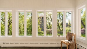 A room with large windows, a radiator, a chair, and a table.