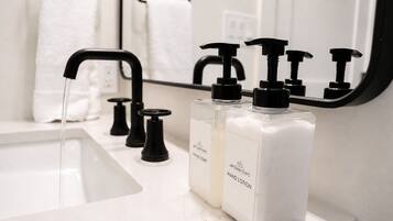 Un baño con lavamanos blanco, grifos negros y dos botellas de jabón de manos y loción con la etiqueta 'Artisan Stays'.