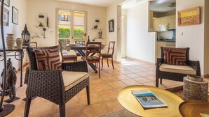 Un vaste espace de vie comprenant une table à manger, des chaises et un canapé. On peut apercevoir la cuisine à travers une porte ouverte.
