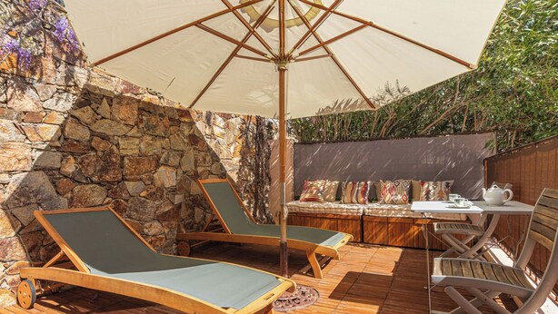 Un espace extérieur ensoleillé, aménagé avec un mur en pierre, une terrasse en bois et une table entourée de chaises.