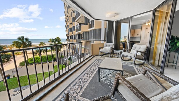 Un balcon avec vue sur la plage, un coin repas avec des chaises et une table, et un espace cuisine.