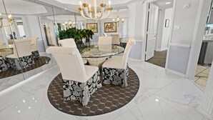 Un coin repas avec une table en verre, des chaises à motifs, un lustre et un grand miroir.