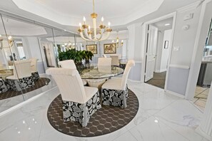 A dining area with a glass table, patterned chairs, a chandelier, and a large mirror. - First-Floor Coastal Retreat at Maisons Sur Mer (Myrtle Beach)