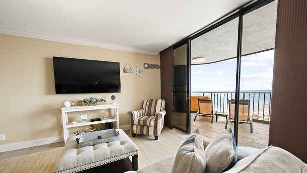 Een woonkamer met een flatscreen televisie, een gestreept fauteuil, een bank en een balkon met uitzicht.