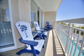 Un balcon avec des fauteuils Adirondack, une table et une vue sur une piscine et une plage.