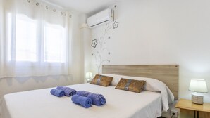 A hotel room with a large bed, a wall-mounted air conditioner, a nightstand with a lamp, and a window with sheer curtains. - Mi Capricho by Interhome (Calafell)