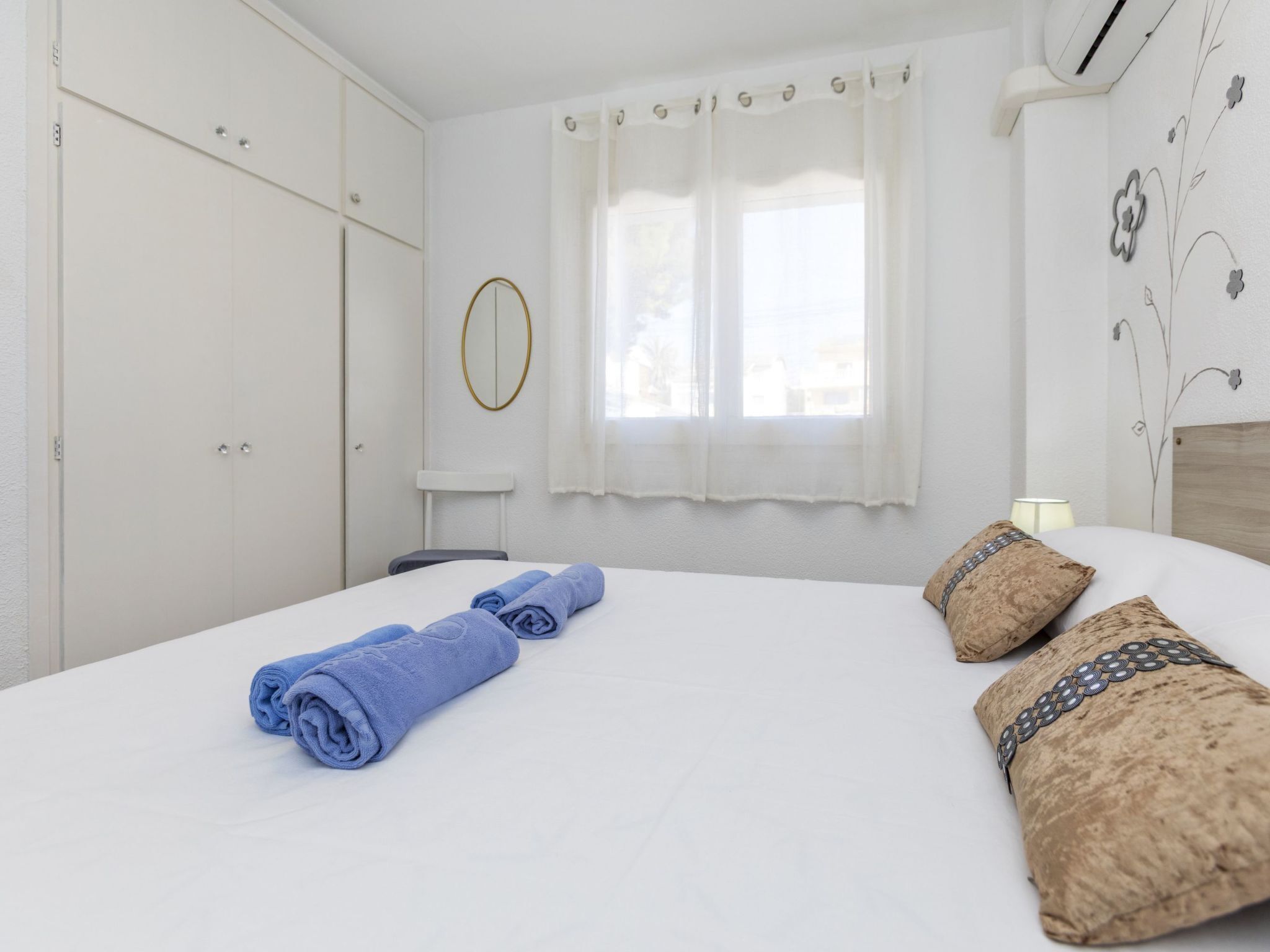 A neatly made bed with rolled towels, a bedside lamp, and a wall with a floral design.