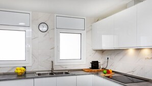 A modern kitchen with white cabinets, a marble backsplash, a clock, and a coffee machine. - Mi Capricho by Interhome (Calafell)