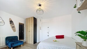 Ein Schlafzimmer mit einem Bett, einem blauen Sessel, einem Holzschrank, einer Tür und einer Wanddekoration.