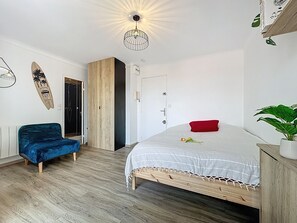Een slaapkamer met een bed, een blauwe stoel, een houten garderobe, een deur en een decoratie aan de muur.