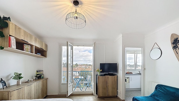 Ein Zimmer mit einem Bett, einem blauen Sofa, einem Fernseher, einem Holzschrank und einem Balkon mit Blick.