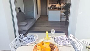 Ein Essbereich mit einem Tisch für zwei Personen, ausgestattet mit einem gewebten Korb mit Käse, zwei gemusterten Tellern und einem Glas Wasser.