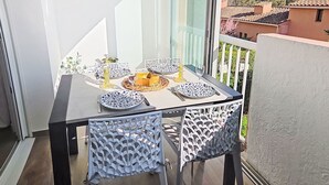 Ein Balkon mit Esstisch, weißen Stühlen und Blick auf Gebäude und Bäume.