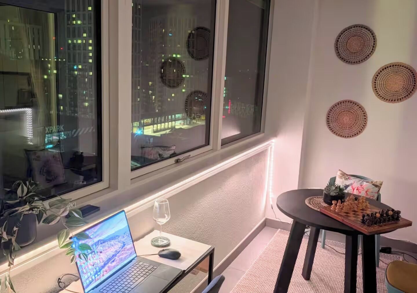 A room with a laptop on a small table, a glass of water, and a chessboard on a side table.