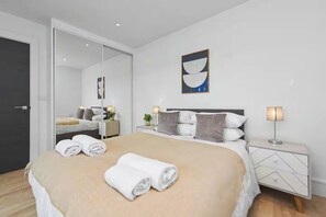 A modern hotel room with a large bed, bedside tables, a mirror, and a painting on the wall. - Fully furnished 1-bedroom apartment in a prime Wembley location (Wembley)