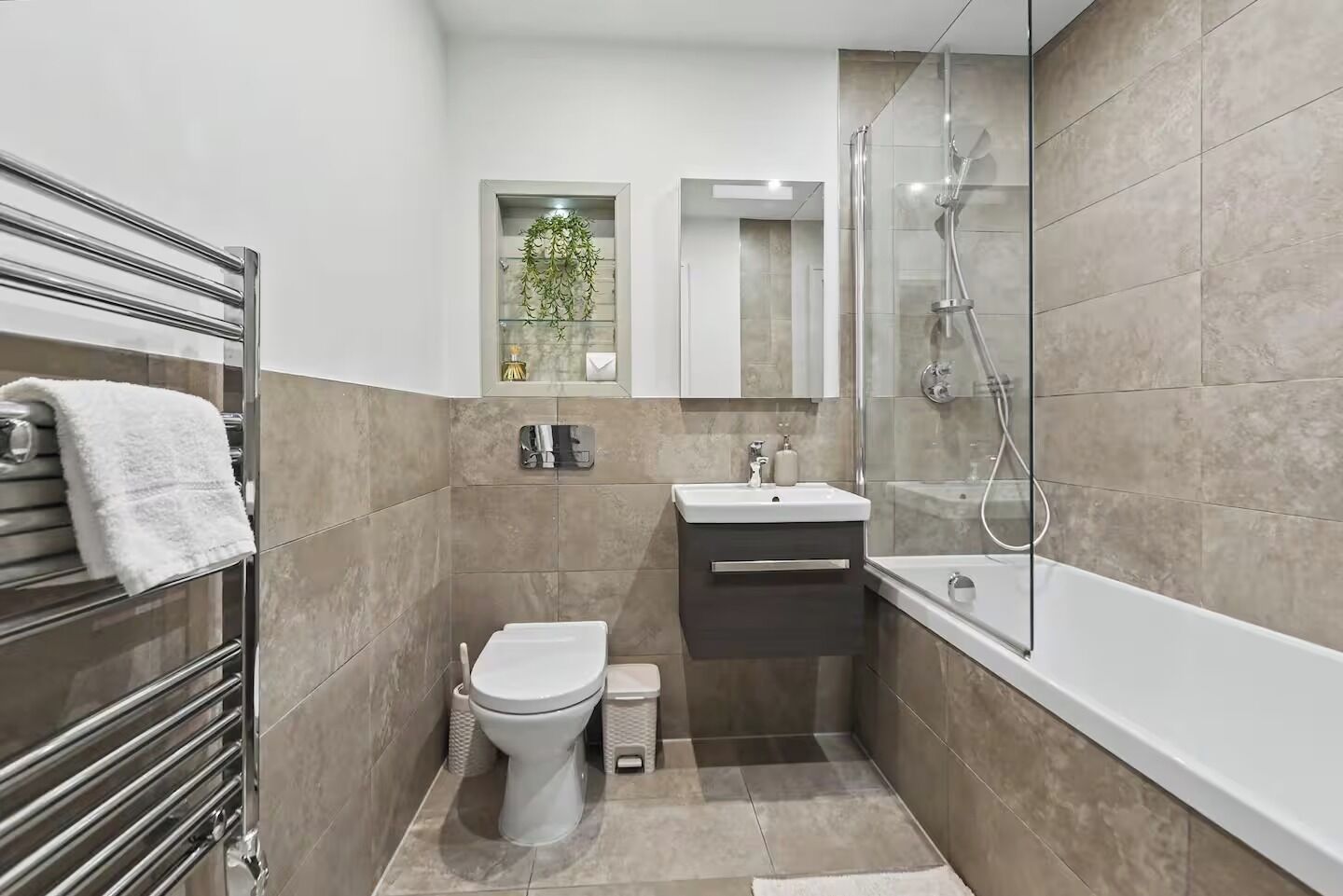 Une salle de bain moderne avec une douche à parois de verre, des toilettes blanches, un lavabo et un porte-serviettes.