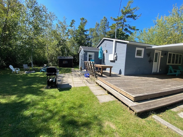 A backyard with a deck, a grill, and a small shed.