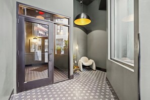 Eine Hotelhalle mit einem gemusterten Boden, einem Glastür-Eingang, einer modernen Pendelleuchte und einem kleinen weißen Sessel.