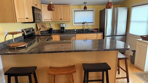 A kitchen with wooden cabinets, a granite countertop, a stainless steel refrigerator, and a bar stool. - Quaint 2-bedroom house overlooking Lake Winnipesaukee in welcoming Gilford (Gilford)