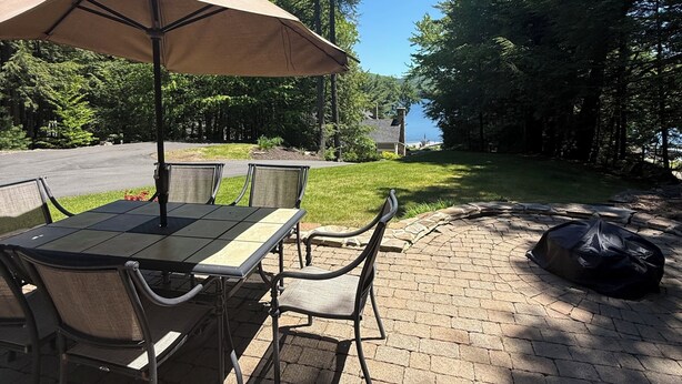 A patio with a table and chairs, an umbrella, and a view of a lake. - Quaint 2-bedroom house overlooking Lake Winnipesaukee in welcoming Gilford (Gilford)