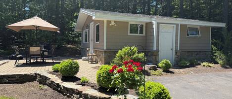 A single-story mobile home with a patio area, outdoor seating, and a stone retaining wall with landscaping.