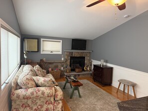A living room with a fireplace, a sofa, a television, and a ceiling fan.