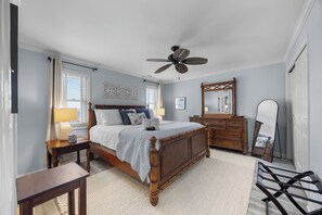 A bedroom with a wooden bed, a ceiling fan, a dresser, and a mirror. - Mayor's Penthouse: Oceanfront luxury w/elevator 4BR (Carolina Beach)
