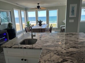 A kitchen with a large island, a dining area with a view of the ocean, and a ceiling fan. - Mayor's Oceanfront Penthouse 4BR w/Elevator in Carolina Beach (Carolina Beach)
