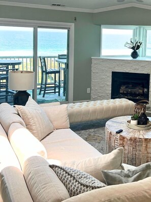 A living room with a large sectional sofa, a fireplace, a round coffee table, and a view of the ocean through large sliding glass doors. - Mayor's Penthouse: Oceanfront luxury w/elevator 4BR (Carolina Beach)