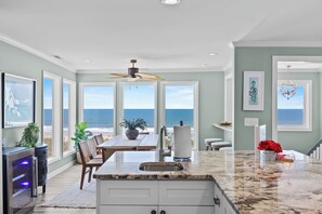 A kitchen with a large island, a dining area with a view of the ocean, and a ceiling fan. - Mayor's Penthouse: Oceanfront luxury w/elevator 4BR (Carolina Beach)