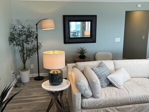 A living room with a sofa, a lamp, a potted plant, and a framed mirror. - Mayor's Oceanfront Penthouse 4BR w/Elevator in Carolina Beach (Carolina Beach)