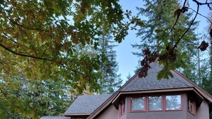 A two-story house with a deck, a covered outdoor seating area, and a stone pathway leading to the entrance. - Eco-Garden: Rural Beauty in recreation heaven. (Central Kootenay E)