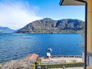 Vista sul lago con un molo, un piccolo edificio e montagne sullo sfondo.