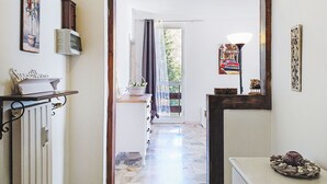 Un corridoio con pavimento piastrellato, un termosifone, un armadietto bianco, un quadro incorniciato e un elemento decorativo a parete.