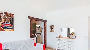 Ett vardagsrum med en soffa, ett matbord, en vit byrå och en tavla som föreställer en bil.