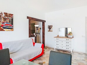 A living room with a sofa, a dining table, a white dresser, and a painting of a car. - Apartment Olli by Interhome (Porto Ceresio)