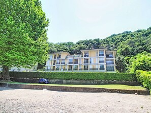 A multi-story building with balconies, surrounded by lush greenery and a well-maintained hedge. - Apartment Olli by Interhome (Porto Ceresio)