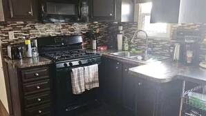 A kitchen with dark wood cabinets, a black stove, and a tiled backsplash. - 30KM to Niagara Falls, Sun Retreat Resort, Private Beach Access/View. Sleep 8 (Port Colborne)