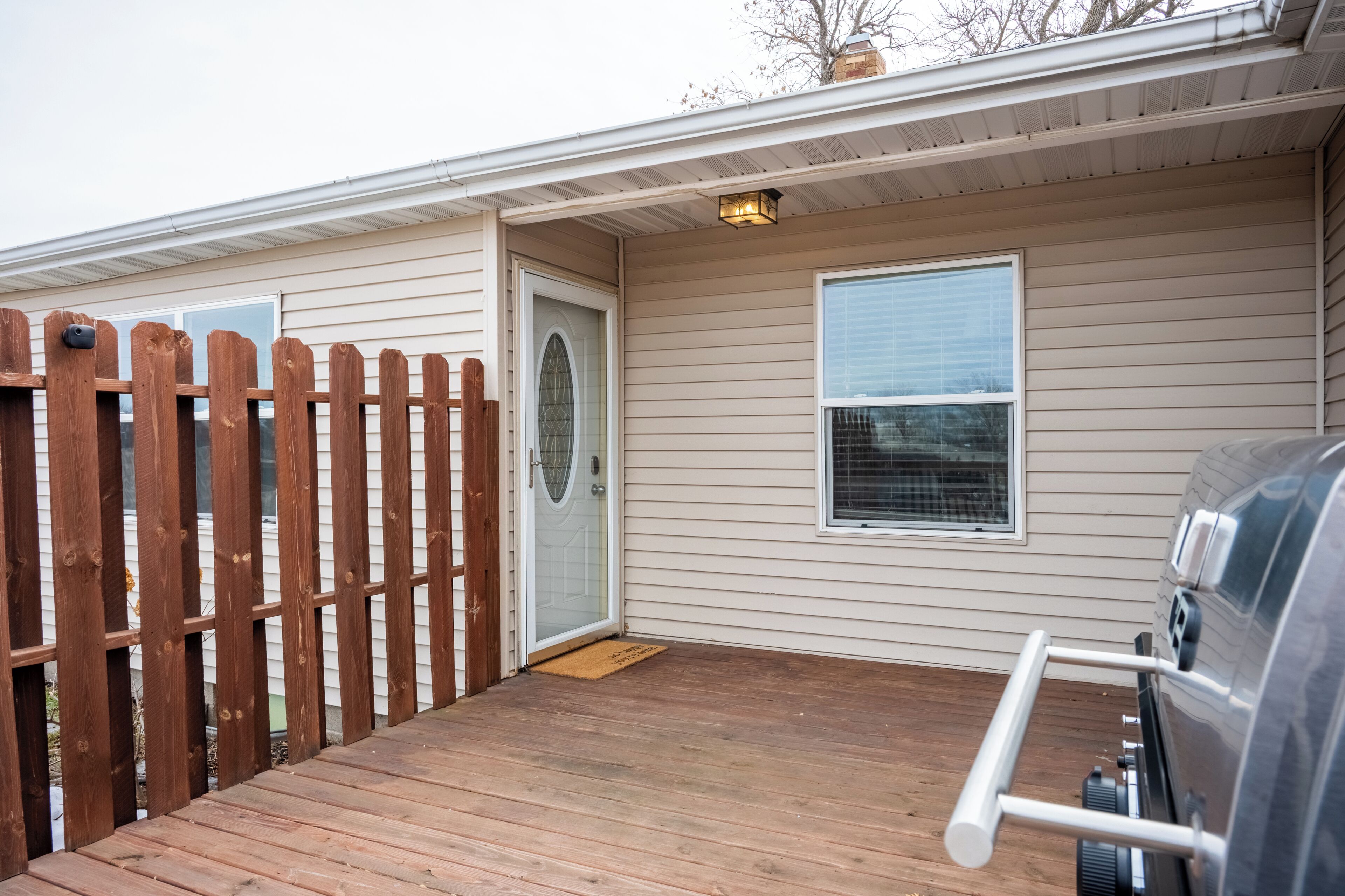 A covered deck area with a wooden fence, a door, a window, and a grill.