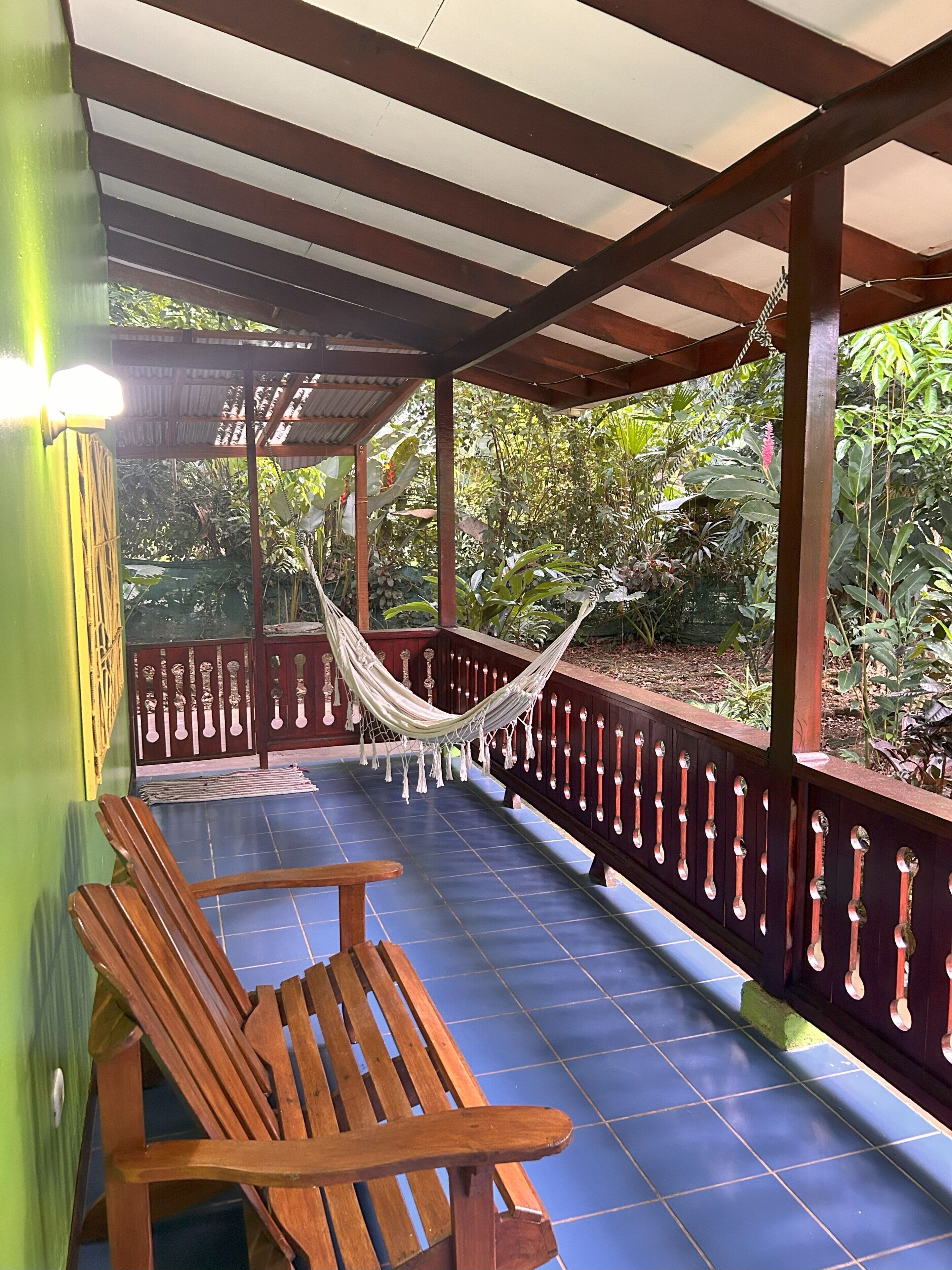 A covered outdoor area with a hammock, wooden benches, and a railing.