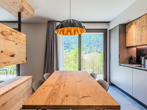 Une cuisine moderne avec une table en bois, un luminaire suspendu et une vue sur une zone boisée.
