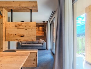 Un intérieur moderne avec une table à manger en bois, un canapé gris et une grande fenêtre donnant sur un paysage verdoyant.