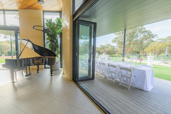 A modern indoor space with a grand piano, a large window, and a table set for dining.