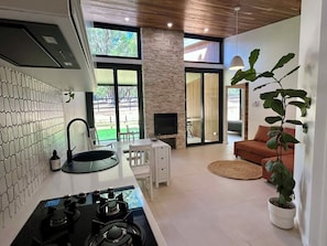 A modern kitchen with a gas stove, a sink, and a large window overlooking a garden.