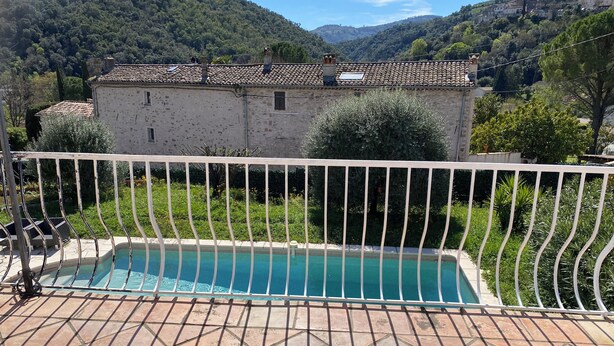 Una piscina con barandilla de metal blanco, un patio de piedra y vistas a una ladera con edificios.